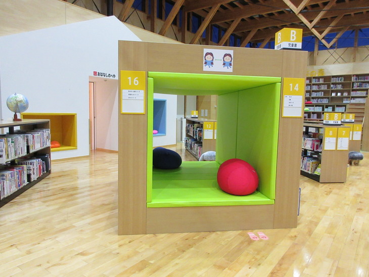 緑色のマットと赤と黒のクッションを設置したキューブ状の読書スペースの写真