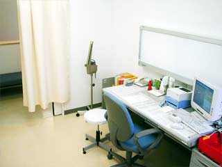 机の上にパソコンや器具などが並んでいる、明るい診察室の様子の写真