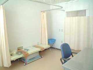 クリーム色のカーテンが入り口とベッドの周りにかかっている、明るい診察室の写真