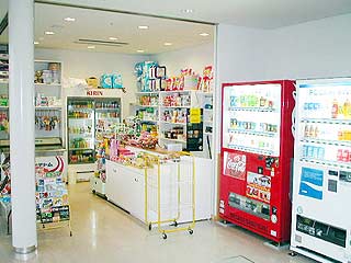 手前に自動販売機が並び、奥に様々な商品が並んだ棚がある売店の写真